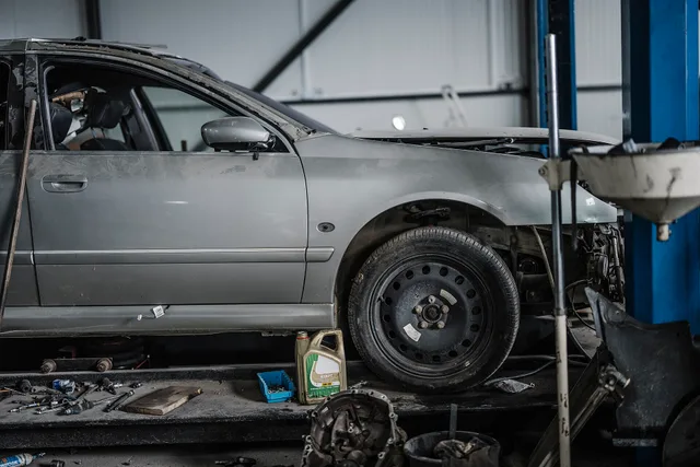 A car is on a lift in an auto shop. Mechanics are working on it while tools and equipment are scattered on the ground. The shop is filled with various items related to car repair. Starting an auto repair shop: the real startup costs and how owners fund them
